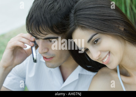 Young couple, woman leaning head against man while man uses cell phone, head and shoulders, portrait Stock Photo