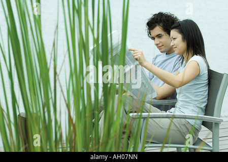 Young couple reading newspaper together by edge of lake Stock Photo
