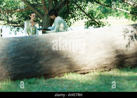 Couple with laptop, tree trunk in foreground Stock Photo