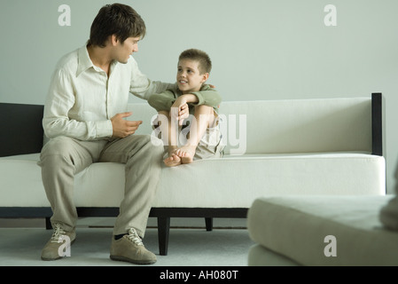 Boy and father sitting on sofa, talking Stock Photo