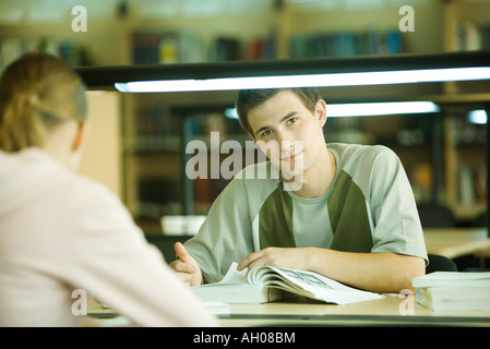 Students studying in university library, teen boy smiling at camera