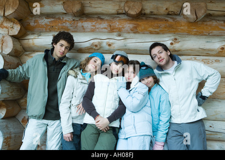 Group in winter clothes standing together, leaning against log wall, three quarter length, portrait Stock Photo