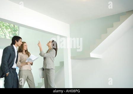 Female real estate agent showing house to young couple, pointing to ceiling Stock Photo