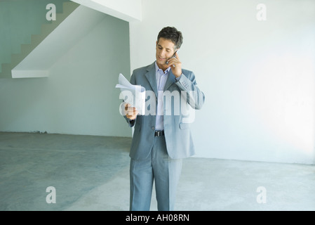 Well-dressed man looking at blueprints, using phone Stock Photo