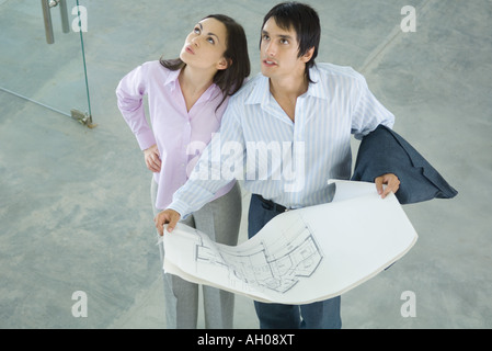 Young couple holding blueprints, looking up, high angle view Stock Photo