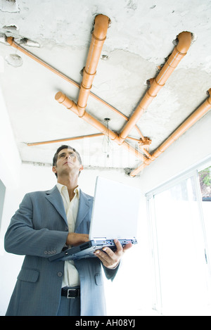 Well-dressed man using laptop, inspecting unfinished home interior Stock Photo