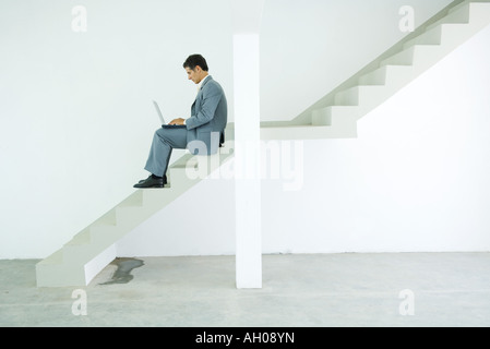 Man in suit sitting on stairs, using laptop Stock Photo