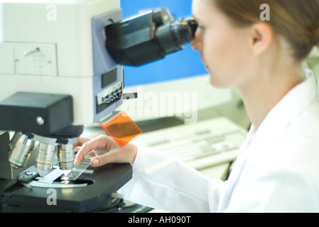 Young female scientist placing slide in microscope Stock Photo