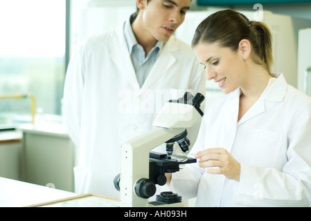 Female lab worker placing slide under microscope, male colleague looking over shoulder Stock Photo