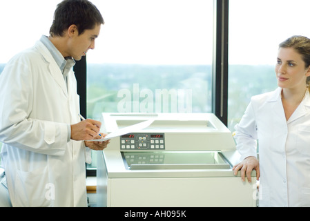 Male and female lab workers standing next to lab machine Stock Photo