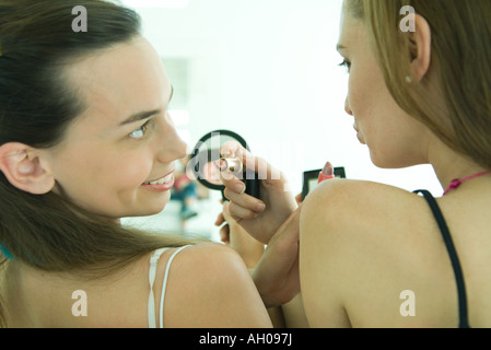 Two young friends putting on makeup, looking at each other, rear view