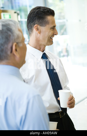 Business associates smiling, holding hot beverages, side view Stock Photo