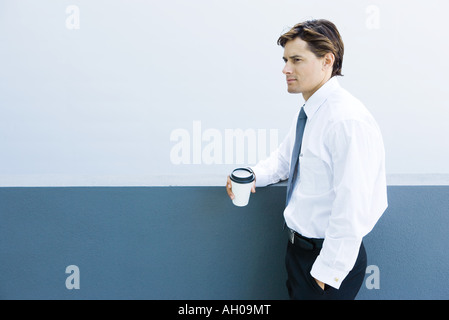 Young businessman standing, holding hot beverage, hand in pocket Stock Photo