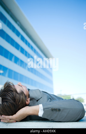 Businessman lying on ground outdoors, hands behind head, cropped view Stock Photo