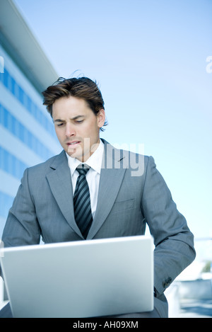 Young businessman outdoors, using laptop computer, looking down Stock Photo