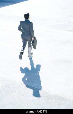 Young businessman running outdoors, carrying briefcase, full length, rear view Stock Photo