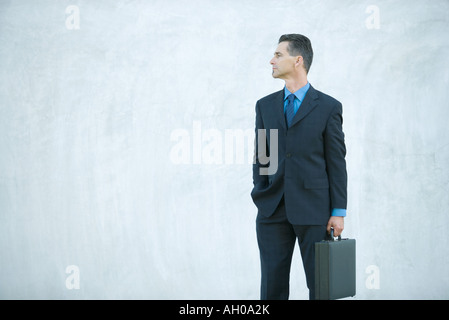 Businessman standing, carrying briefcase, looking away Stock Photo