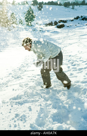 Young man bending over in snow, dodging snowball, full length Stock Photo