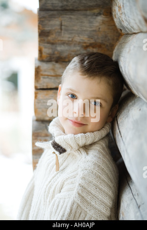 Boy leaning against wood cabin, smiling at camera Stock Photo