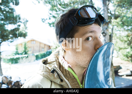 Young man kissing snowboard, glancing at camera Stock Photo