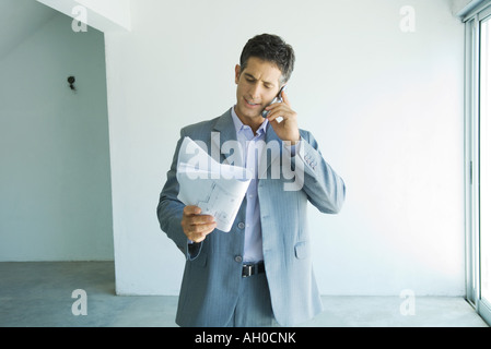 Man in suit looking at blueprints, using cell phone Stock Photo
