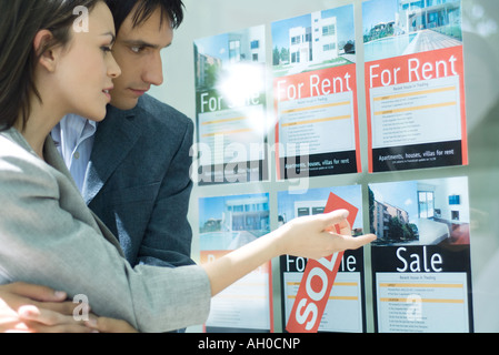 Couple looking at properties in window of real estate agency Stock Photo