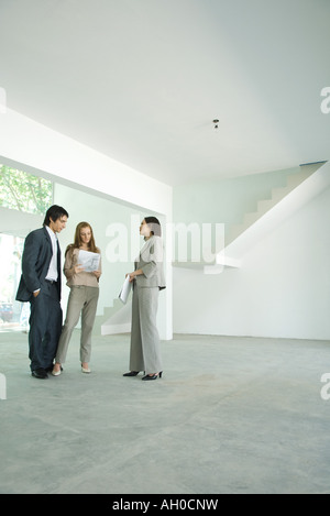 Female real estate agent standing in empty home interior with young couple, full length Stock Photo