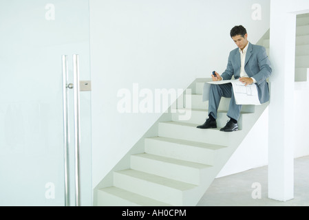 Man sitting on stairs, looking at blueprints Stock Photo