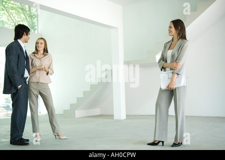 Female real estate agent standing in empty home interior with young couple, full length Stock Photo