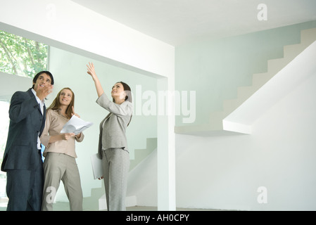 Female real estate agent standing in empty home interior with young couple, full length Stock Photo