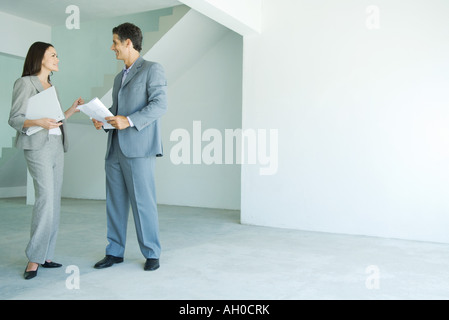 Man and woman in suits standing in empty home interior, smiling, face to face, full length Stock Photo