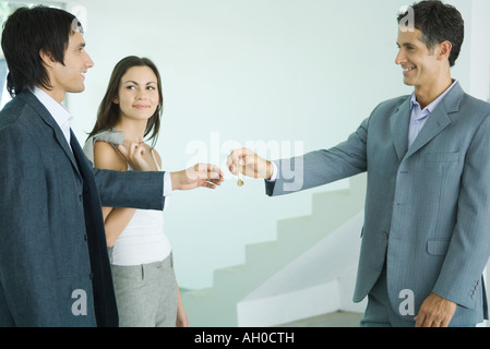 Real estate agent handing keys to young couple Stock Photo