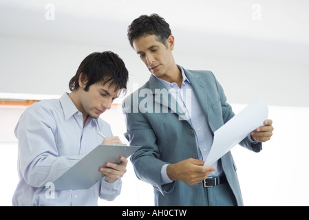 Young man writing on clipboard, mature man looking over shoulder Stock Photo