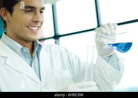 Male scientist transfering liquid from flask to cylinder, smiling Stock Photo