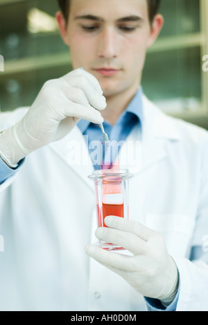 Young male lab worker dipping slide into liquid in beaker Stock Photo