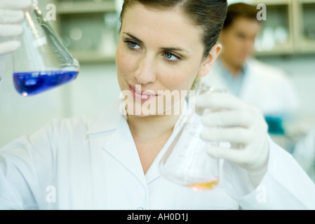 Young woman working in scientific laboratory, holding up flasks Stock Photo