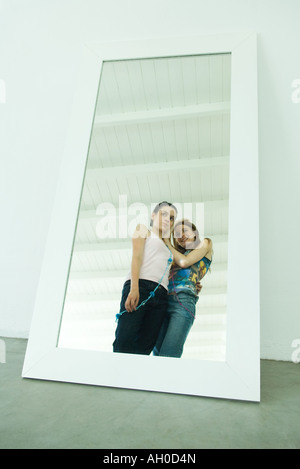 Two young friends standing together, looking at selves, reflected in mirror Stock Photo
