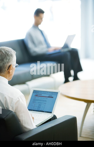 Two businessmen using laptops in lobby, focus on mature man in foreground Stock Photo