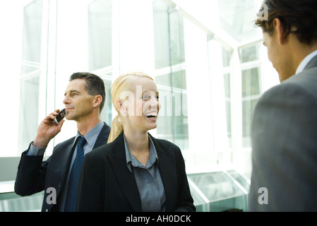Business colleagues in hallway, woman laughing, man in background using cell phone Stock Photo