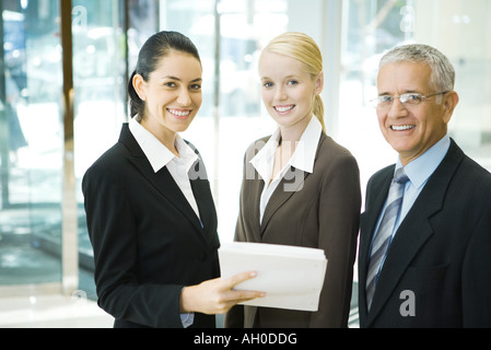 Business associates smiling at camera, one woman holding stack of documents Stock Photo