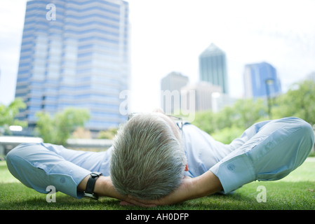 Businessman lying on grass, hands behind head Stock Photo