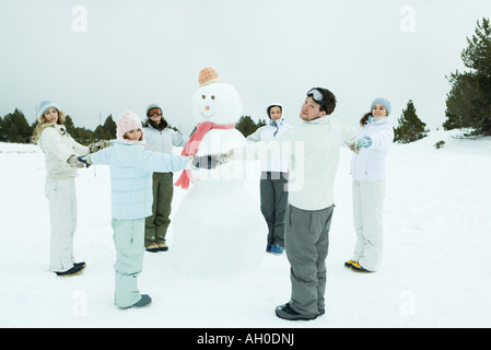 Young friends standing in circle around snowman, holding hands, smiling at camera Stock Photo