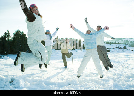 Young friends jumping in the air, dressed in winter clothing, smiling at camera Stock Photo