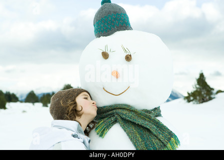 Girl leaning against snowman, looking away, portrait Stock Photo
