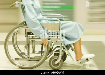 Cropped view of man using wheelchair, dressed in hospital gown, blurred motion Stock Photo