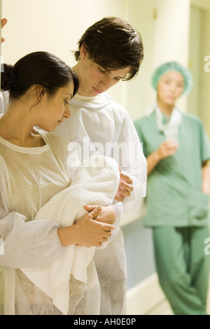 Couple standing, looking at newborn baby together, doctor in background Stock Photo