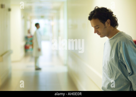 Male patient standing in hospital corridor, looking down, side view Stock Photo