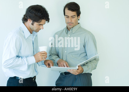 Two businessmen standing, looking at binder, waist up Stock Photo