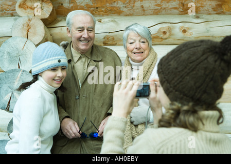 Teenage girl photographing grandparents and sister with digital camera, waist up