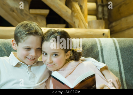 Boy and girl reading together, smiling at camera, cheek to cheek Stock Photo